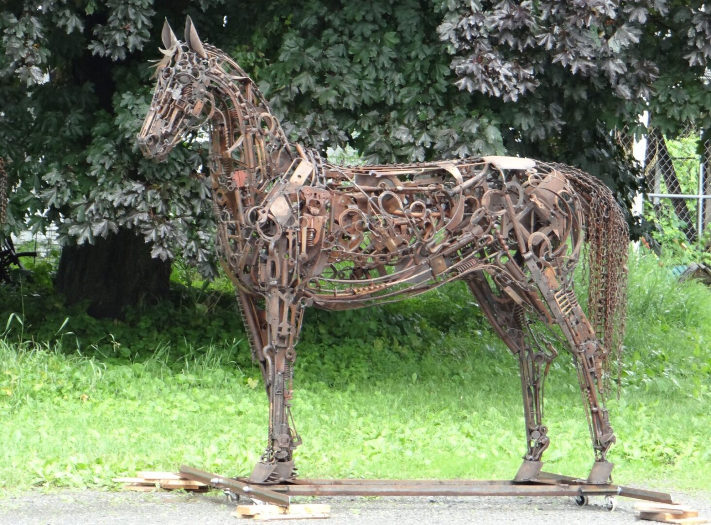 A horse made of metal is standing in a grassy area.